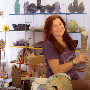 Karin Seifried sitzt in ihrem Atelier und zeigt eine Vase her.